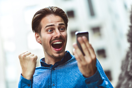 Excited man looking at his smartphone reading good news message email.の写真素材