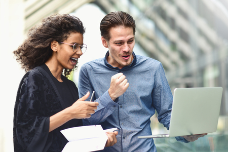 Business man and woman working on laptop together on building background in city outdoor feeling happy.の写真素材