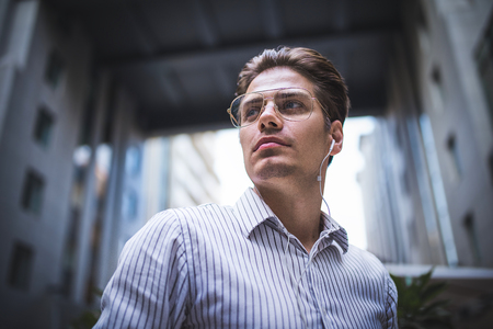 Happy handsome businessman at street with headphones looking through shoulder.