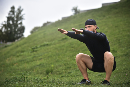 Young caucasian man performing squats before jogging on footpath in park.の写真素材