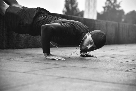 Young bearded sportsman makes workout in a park, doing a series of push ups outdoor.の写真素材