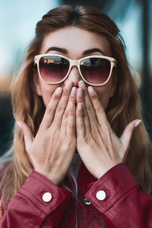 Closeup portrait of beautiful pensive blonde white Caucasian girl woman, weared in red jacket outside in city street, lifestyle portrait conceptの写真素材