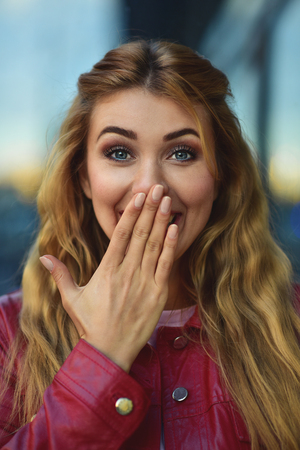 Closeup portrait of beautiful pensive blonde white Caucasian girl woman, weared in red jacket outside in city street, lifestyle portrait conceptの写真素材
