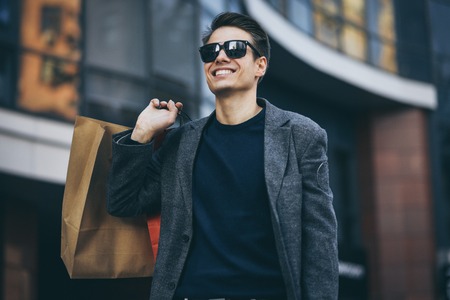 Serious cool guy with sunglasses and paper bags walking at street.の写真素材