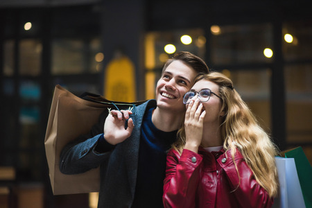 Beautiful couple with shopping bags is talking and smiling while doing shopping in the mall focus on...