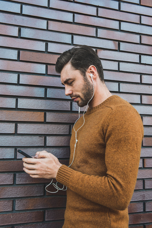Smiling man listening to music on headphones and leaning against brick wall.の写真素材