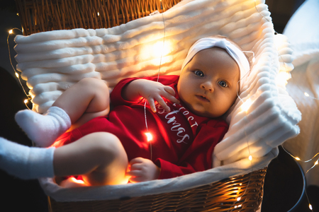 Lovely, beautiful newborn girl lying in basket in a white hat, new year and Christmas decorations, garland on the wall, with a flashlight. card, text. toning.の写真素材