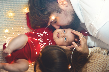 Top view. Mother and Father Kisses Baby in Bed. Little Newborn Child in White Bed. Parenthood Concepts. Love and Happiness. Taking Care of New Life.の写真素材