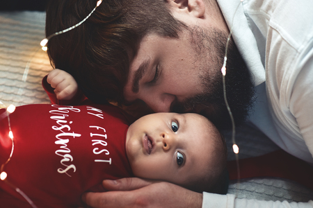 A young father kisses his newborn daughter. Father and newborn baby closeup. Father and newborn lying on the bed.の写真素材