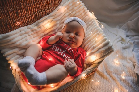 A cute newborn baby in xmas clothes sleeping in a basket on the floor against a Christmas decoration. New Year's Eve.の写真素材