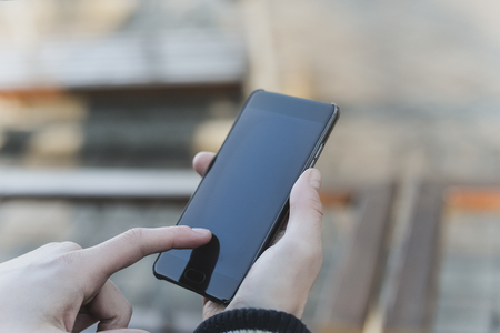 A Guy in a warm jacket with a smartphone in his hands, a sunny day.の写真素材