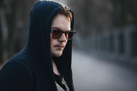 Portrait of fashion man in a black sweater with a hood and sunglassesの写真素材