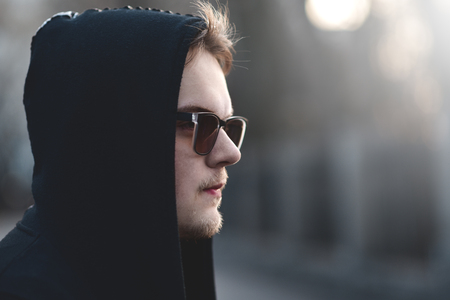 Portrait of fashion man in a black sweater with a hood and sunglassesの写真素材