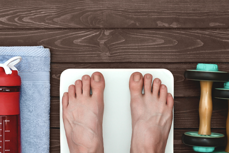 The guy becomes on a scale after training, nearby lie dumbbells and a bottle of water on a towel.の写真素材