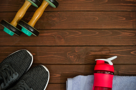 Fitness and healthy active lifestyle, background concept. Training sneakers, dumbbells, scales, a bottle of water on a wooden backgroundの写真素材