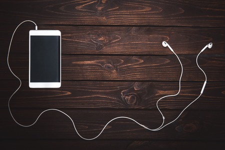 white smartphone with white headphones on wooden background- Image.Listening to musicの写真素材