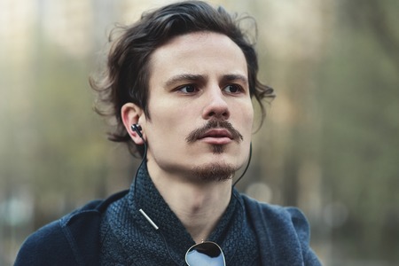 Handsome young curly hair man listening to music and thinks about something important for him. He is...