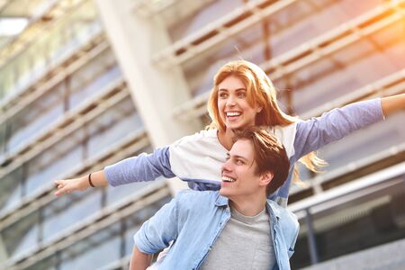 Man giving his pretty girlfriend a piggy back at street smiling at each other on a sunny day.の写真素材