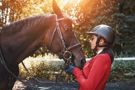 A young girl talking and kissing her horse. She loves the animals and joyfully spends her time in their environment.の写真素材
