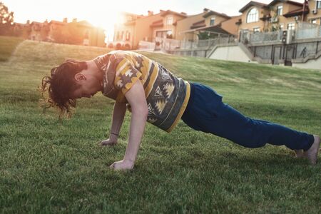 Sport. Athlete doing push-ups at sunset in the park . skinny guy exercising and trying to get fit.