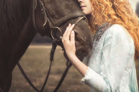love for animals. young Woman with no face dressed in an elegant vintage dress, gently cuddling a horse, stroking his head.の写真素材