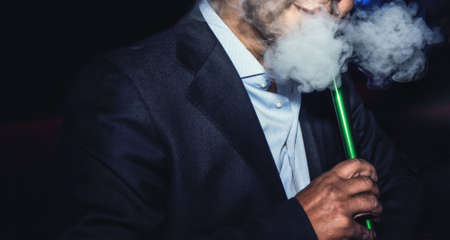a man with no face smokes a hookah slowly exhaling smoke at the nightclubの写真素材