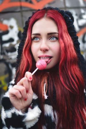 Portrait of a young beauty teen girl in a hoodie with a delicious pink lollipop, posing against a wall of graffiti. Positive Emotions. Urrban styleの写真素材