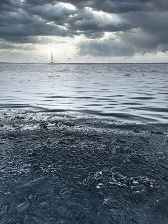 Blue winter ice a winter scene with blue ice with a lighthouse glowing in the distance, against a background of beautiful overcast clouds.の写真素材
