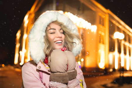 portrait of a charming woman on a snow-covered street, wearing a winter jacket and hoodie, smiling...