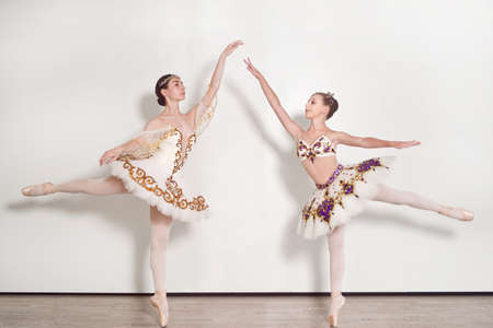 Two ballerinas young practicing ballet poses against a white backgroundの写真素材