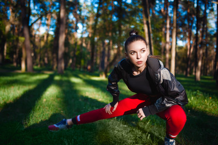 Focused young woman performs a stretch routine in a serene forest, embracing a healthy lifestyleの写真素材