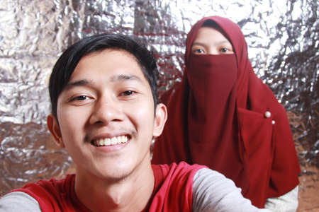Asian man and woman's portrait taking a photo together holding the camera against a silver paper background. togetherness in a romantic and happy relationshipの写真素材