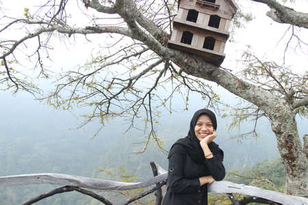 portrait of an Asian woman with a happy expression posing under a pigeon cage. enjoy a hilltop vacation on the weekend.の写真素材