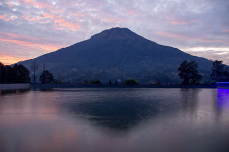 Embung Kledung is a tourist destination in Temanggung, Indonesia. a fish pond containing koi with a background of Sindoro mountain. clear sunrise sky with reflection on the artificial lakeの写真素材
