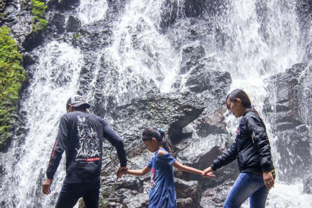 Batu City, Indonesia. November 2020. the family is enjoying the freshness of the Watu Lumpang waterfall. parents and children are on vacation in fresh natural tourist destinationsのeditorial素材