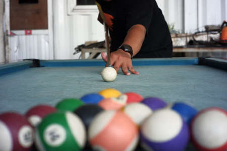 men's hands playing billiards on a blue carpeted table. a portrait of a professional player with a blurry billiard ball foreground. the first step of the billiard game beginsの写真素材