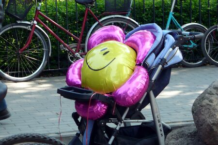 flower-shaped balloon in a stroller colored pink and yellow smiling in the background a few bikesの写真素材