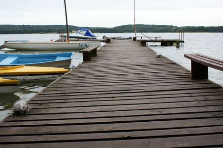 wooden bridge on the lake moored boats sailboat cloudy weather on Masuria in Polandの写真素材