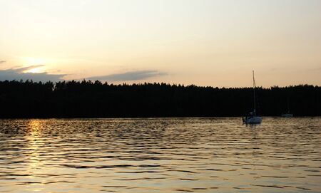 lake Mazury Poland a sailboat sailing on it yacht sunset on the lake with orange sky cloudy clouds red and purple sunの写真素材