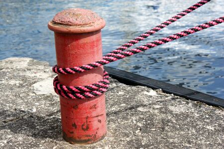 Red sailing hawser mooring rope from yacht in the port on concrete quay