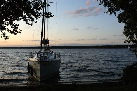 sunset sailing yacht sailboat moored on a dead lake silhouette between the branches of treesの写真素材
