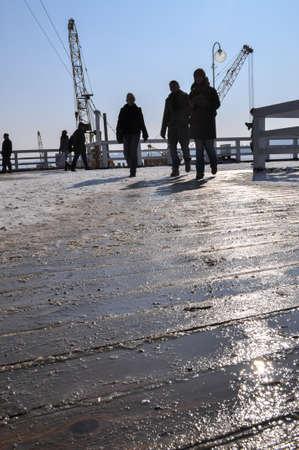 pier under construction oil rig cranes light reflection in wooden wet planks platform people silhouette sunlightの写真素材