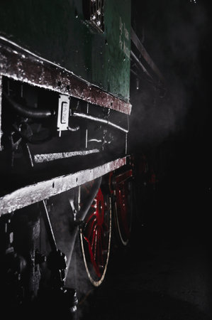 Close-up of an antique green railway car with red wheels, dim light in darkness, earthy nightの写真素材