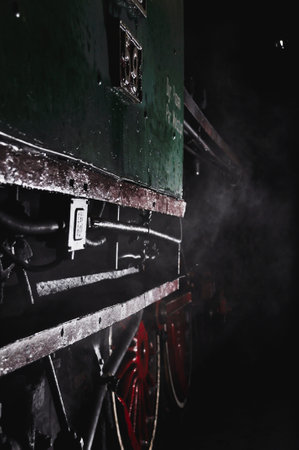 Close-up of an antique green railway car with red wheels, dim light in darkness, earthy nightの写真素材