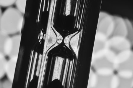 A black-and-white hourglass close-up measuring time with flowing sand