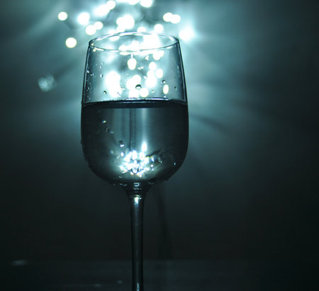 A glass filled with water, shades of blue, white bokeh from lights in the background, small light sources.の写真素材