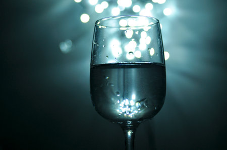 A glass filled with water, shades of blue, white bokeh from lights in the background, small light sources.の写真素材