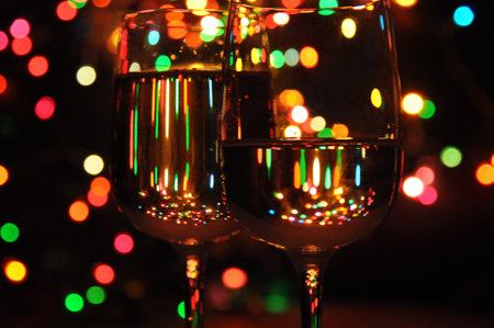 transparent wine glasses filled with water, with colorful Christmas lights on a tree in the backgroundの写真素材