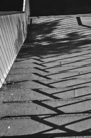 Monochromatic photo of stairs, close-up of shadows cast on the stairs from the railing black and...