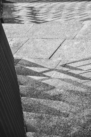 Monochromatic photo of stairs, close-up of shadows cast on the stairs from the railing black and...